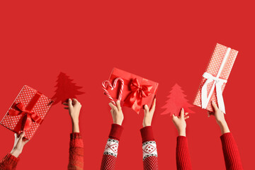 Hands holding Christmas gifts and paper fir trees on red background