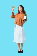 Beautiful Asian woman with glass and bottle of wine on blue background