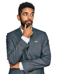 Young african american man wearing business clothes with hand on chin thinking about question,...