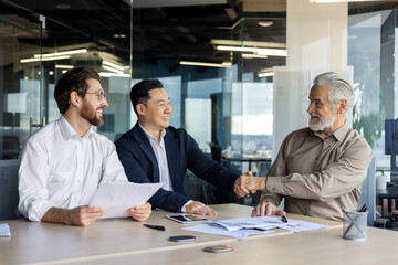 Three male businessmen having a business meeting in the office, shaking hands and smiling, successful negotiation.