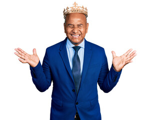 Hispanic middle age man wearing king crown celebrating mad and crazy for success with arms raised...