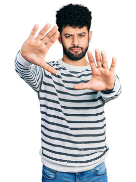 Young arab man with beard wearing casual striped sweater doing frame using hands palms and fingers, camera perspective