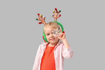 Cute little girl in reindeer horns with snowflake on light background