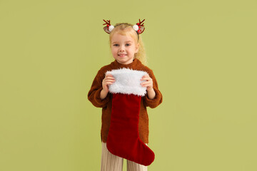 Cute little girl with Christmas sock on green background