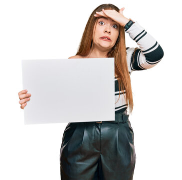 Young beautiful redhead woman holding blank empty banner stressed and frustrated with hand on head, surprised and angry face