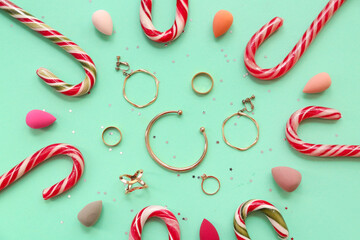 Christmas candy canes with jewelry and cosmetic sponges on turquoise background - obrazy, fototapety, plakaty