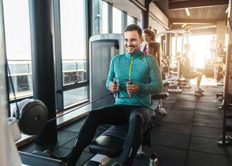 Happy male athlete doing rowing workout in the gym. Handsome man doing seated cable rows during...