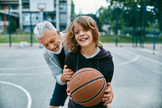 Grandfather teaching his grandson how to play basketball at an outdoor basketball court