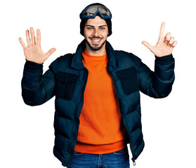 Young hispanic man with beard wearing snow wear and sky glasses showing and pointing up with fingers number seven while smiling confident and happy.