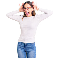 Beautiful brunette young woman wearing casual white sweater and glasses smiling cheerful playing peek a boo with hands showing face. surprised and exited