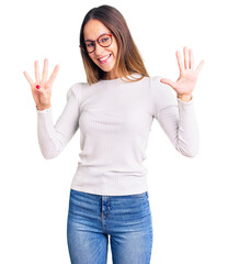 Beautiful brunette young woman wearing casual white sweater and glasses showing and pointing up...