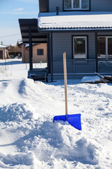 Blue snow shovel against the background of a snowdrift in front of the porch of a house