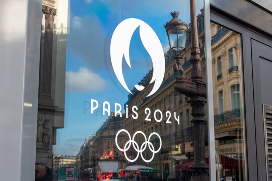 Paris, France - 6 d&eacute;cembre 2023: Gros plan du logo symbole des Jeux olympiques d'&eacute;t&eacute; de Paris 2024 sur une vitre avec le reflet d'une rue de Paris