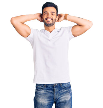 Young handsome hispanic man wearing casual clothes relaxing and stretching, arms and hands behind head and neck smiling happy