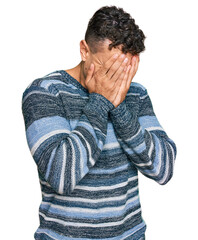 Hispanic young man wearing casual clothes with sad expression covering face with hands while...