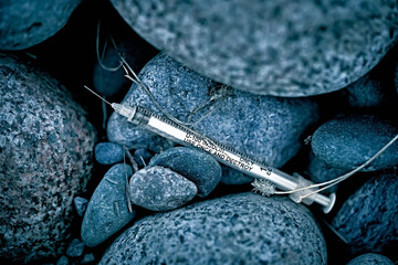 Discarded among the rocks in a park on a city street is a used syringe.