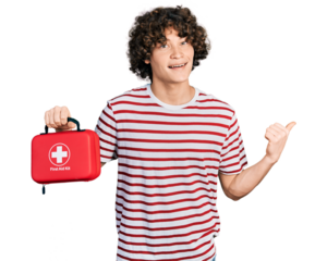 Caucasian teenager holding first aid kit pointing thumb up to the side smiling happy with open mouth