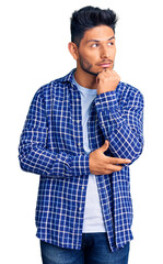 Handsome latin american young man wearing casual shirt serious face thinking about question with hand on chin, thoughtful about confusing idea