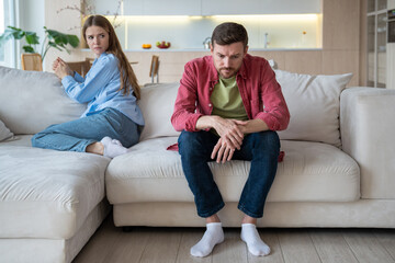 Gloomy upset passive man sitting on sofa apathetically looking on floor with blank stare, and...