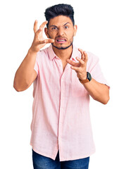 Handsome latin american young man wearing casual summer shirt shouting frustrated with rage, hands trying to strangle, yelling mad