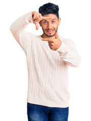 Handsome latin american young man wearing casual winter sweater smiling making frame with hands and fingers with happy face. creativity and photography concept.
