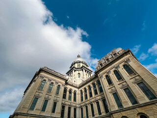 Naklejka premium Rear views of the Illinois State Capitol Building in Springfield, Illinois, USA. Cloudy blue skies overhead. Sunlight shines down upon the dome of the building.