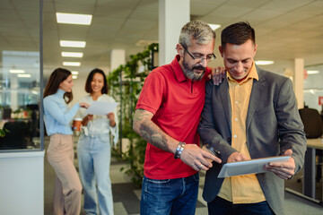 Middle aged colleagues chatting in an office and using a tablet - Powered by Adobe