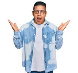 Young latin man wearing casual clothes and glasses celebrating victory with happy smile and winner...