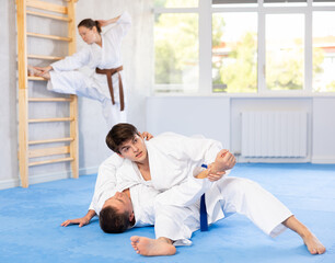 Two males practicing judo together on sports mats under the guidance of a trainer
