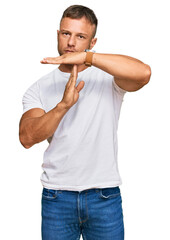 Handsome muscle man wearing casual white tshirt doing time out gesture with hands, frustrated and...