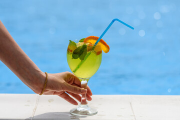 Cocktail in a female hand on the background of the pool
