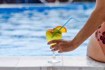 Cocktail in a female hand on the background of the pool