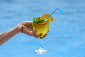Cocktail in a female hand on the background of the pool