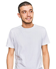Fototapeta premium Hispanic young man wearing casual white t shirt looking away to side with smile on face, natural expression. laughing confident.