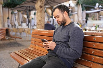 Man looking at cell phone sitting on bench in park