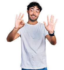 Fototapeta premium Hispanic young man with beard wearing casual white t shirt showing and pointing up with fingers number eight while smiling confident and happy.