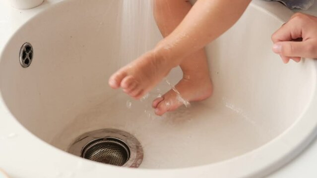 Kid, child girl washes feet in kitchen sink under running water. High quality FullHD footage