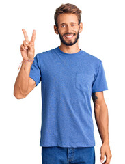 Handsome blond man with beard wearing casual clothes smiling with happy face winking at the camera doing victory sign. number two.
