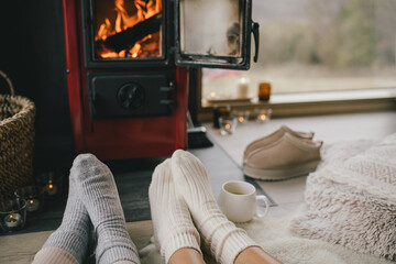 Two women sitting by the fireplace in knitted socks, drinking tea in cozy log cabin.