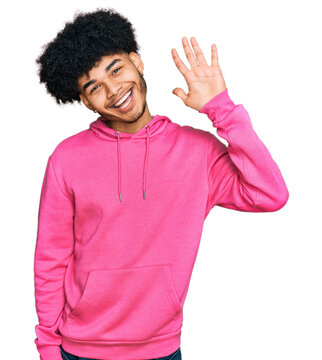 Young African American Man With Afro Hair Wearing Casual Pink Sweatshirt Waiving Saying Hello Happy And Smiling, Friendly Welcome Gesture