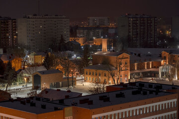Widok miasta nocą w śniegu . Oświetlone historyczne budynki i nowoczesne bloki mieszkalne . Jesienna noc w Ostrowcu Świętokrzyskim. - obrazy, fototapety, plakaty
