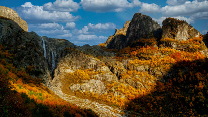 Spectacular autumnal landscape featuring rugged cliffs and a cascading waterfall surrounded by...