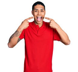 Young hispanic man pointing mouth with fingers celebrating crazy and amazed for success with open...
