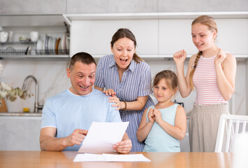 Obraz na płótnie Canvas Joyful family gets acquainted, considers printed plan of future new apartment, housing. Wife claps hands, daughters happily hug father