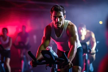 Tuinposter Fit young man in sportswear riding a stationary bike during a cycling class at the gym. © FutureStock