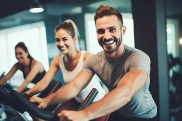 Foto op Canvas Fit young man in sportswear doing a cycling class in a gym with female friends in the background. © FutureStock