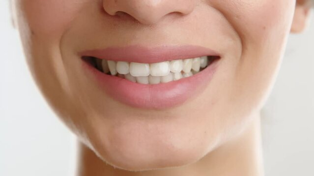 Part of face of young woman with light natural makeup, pretty lips of medium size and beautiful shape, rows of white straight teeth, speeking, smiling. High quality 4k footage