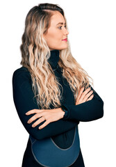 Young blonde woman wearing diver neoprene uniform looking to the side with arms crossed convinced and confident