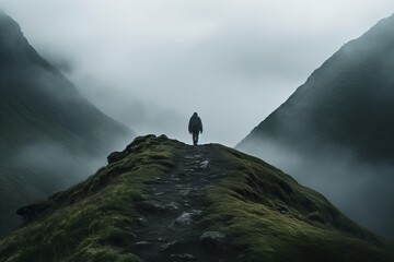Lone figure standing on a rugged hilltop, surrounded by the dramatic and misty mountain landscape, embodying solitude and adventure.