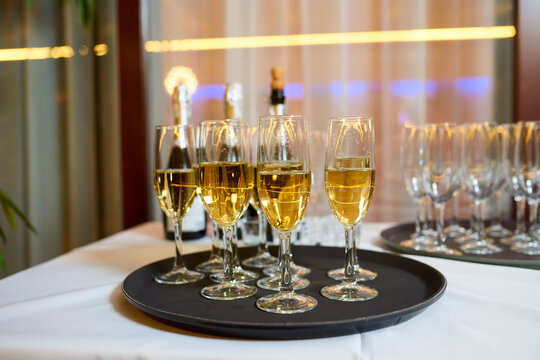 Close-up photo of glasses filled with champagne on a black tray on a white table. New Year, corporate celebration at work, wedding, birthday or Christmas Party.